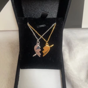 Delat hjärta halsband guld och silver - Två halsband med varsin halva av ett delat hjärta, en i silverfärg och en i guldfärg. Hängena har en blixtformad kant och är perfekta att dela med din bästa vän. Kedjorna är tunna och smidiga, och hängena har en cool, minimalistisk design. Rostfri 