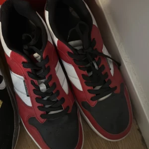 Rödvita sneakers från Jack & Jones - Snygga sneakers från Jack & Jones i rött, vitt och svart. Skorna har klassisk snörning, rund tå och platt sula. Perfekta för dig som gillar streetstyle och vill ha ett par färgstarka skor i garderoben.