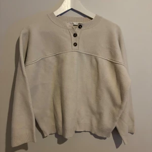 Beige stickad tröja från Zara - Beige stickad tröja från Zara med rund halsringning och tre snygga knappar framtill. Tröjan har en avslappnad passform, ribbade muddar och är långärmad. Perfekt för lager-på-lager under kyliga dagar. Lite nopprig 