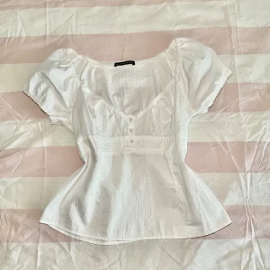 Vit blus från Brandy Melville - Supersöt vit blus från Brandy Melville med korta puffärmar, v-ringning och dekorativa knappar framtill. Blusen har lätt rynkade detaljer vid bysten.Priset kan sänkas!💕