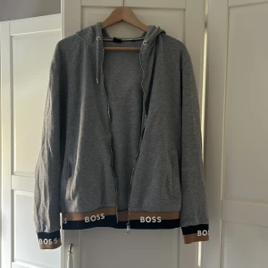 Grå hoodie från BOSS med dragkedja - Snygg grå hoodie från BOSS. Storleken är i ”S” men passar bra ”M” också. Fint skick