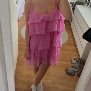 Rosa volangklänning med smala axelband - Säljer en superfin rosa kortklänning med flera lager volanger och smala axelband. Klänningen har en luftig och flowy passform, perfekt för varma dagar. Materialet känns lätt och bekvämt mot huden. Perfekt för dig som gillar färg och volym! Köpt på en marknad i spaninen! 