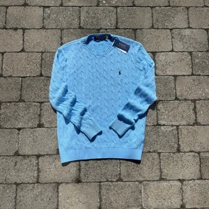 Ljusblå kabelstickad tröja, Ralph Lauren M - Stilren Ralph lauren stickad. Sprillans ny aldrig använd då den inte passade mig. Storlek M färg Ljusblå passform vanlig. Mått 44 och 66cm