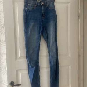 Blå skinny jeans med hög midja - Snygga blå skinny jeans med hög midja och klassisk femficksdesign. Jeansen har en lätt tvättad look och smal passform hela vägen ner. Perfekta att matcha med sneakers eller boots för en cool vardagsstil.