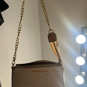  beige väska lik Michael Kors - Supersnygg väska lik Michael kors i en beig och brun färg. Väskan är i använt skick och har en del defekter på självaste bandet. Skriv privat för fler frågor! 