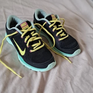 Nike sneakers svart/gul/turkos - Nike sneakers i svart mesh med turkos sula och gula detaljer. Skorna har gula snören, rosa detaljer vid snörhålen och en stor gul Nike-logga på sidan. Perfekta för träning eller en sportig look. Ovandel i syntet och mesh för bra andningsförmåga.