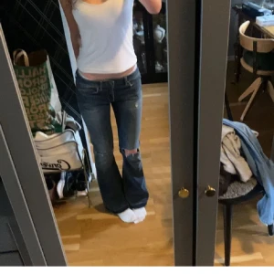Blå bootcut jeans från Dondup - Snygga blå bootcut jeans från Dondup med slitningar och hål på knät. Låg midja och klassisk femficksmodell. Jeansen har fransade benslut och är tillverkade i mjukt denimtyg. Perfekta för dig som gillar en avslappnad och trendig look.
