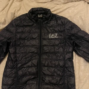EA7 Emporio Armani quiltad jacka tunn dunjacka  - Snygg svart/ mörkblå tunn dunjacka  från EA7 Emporio Armani med logga på bröstet och dragkedja framtill storlek M men skulle tro den passar S också  (HERR) Används till o från. Köpt för cirka 1900 kr men säljs för 350 kronor.