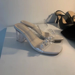 Klara sandaler med pärldetaljer - Säljer ett par trendiga sandaler med transparenta remmar och chunky klack i akryl. Främre remmen är dekorerad med pärlor och små stenar för extra bling. Snygg fyrkantig tå och ljus sula. Perfekta för dig som vill sticka ut med en modern och fräsch look.