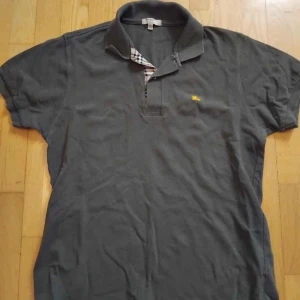 Grön Burberry London slim fit t-shirt - Snygg grön  t-shirt från Burberry London i slim fit-modell. Klassisk pikékrage med rutigt Burberry-tyg på insidan och gul broderad logga på bröstet. Tillverkad i mjuk bomull, perfekt för dig som gillar stilrena detaljer. Den är som en L