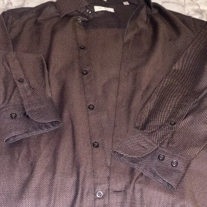 Brun slim fit skjorta These Glory Days - Snygg brun skjorta från These Glory Days i slim fit-modell. Skjortan har ett diskret mönster, klassisk krage och svarta knappar. Tillverkad i 100% bomull och passar perfekt för dig som gillar stilrena detaljer och en smalare passform. Finns extra knappar med 😊