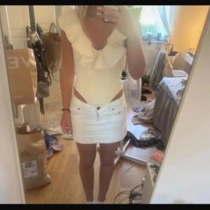 Beige volangtopp/body med djup v-ringning zara - Supersnygg beige body med djup v-ringning och stora volanger längs halsringningen. Toppen är ärmlös och har en figurnära passform som framhäver siluetten. Perfekt för dig som vill sticka ut med en feminin och trendig look. Ny med prislapp 