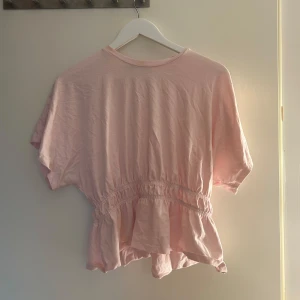 Ljusrosa blus med volang - Söt ljusrosa blus med korta ärmar och volang nedtill. Har en jätteliten fläck där uppe men annars jättebra skick. Använd endast en gång. 