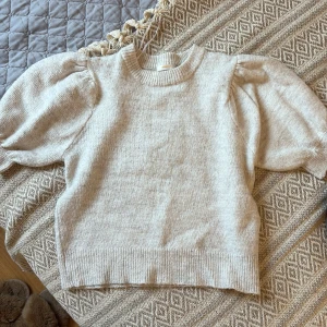 Beige stickad tröja från Gina Tricot - Superfin beige stickad tröja från Gina Tricot med puffiga korta ärmar och ribbade muddar. Perfekt för dig som gillar en enkel men trendig look. Mjuk och skön, passar till allt och ger en stilren vibe.