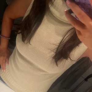 Beige ärmlös stickad polotröja - Inte mina bilder utan hon jag köpte den av!!   Det finns ett mini mini hål på axeln av tröjan som ni ser på sista bilden.                                             Säljer en beige ärmlös stickad polotröja med hög krage. Tröjan har en clean och enkel look, perfekt att styla med jeans eller kjol. Mjuk och skön med ribbade detaljer vid krage och nederkant.