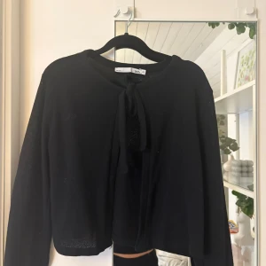 Svart kofta med knyt från 157 - Svart, tunn och stickad kofta från 157 i storlek XS. Koftan har långa ärmar och knyt framtill vid halsen för en söt och enkel look. Perfekt att slänga över en topp eller klänning när det blir lite kyligt. Storlek xs💕