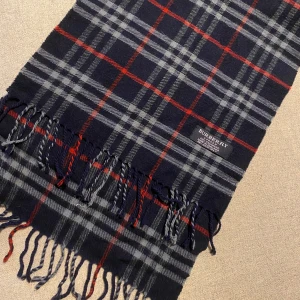 Rutig kashmirhalsduk från Burberry - Snygg halsduk från Burberry i 100% kashmir med klassiskt rutigt mönster i mörkblått, grått och röda linjer. Mjukt material och stilrena fransar i ändarna. Perfekt accessoar för att lyfta din look med lite lyxig London-vibe.