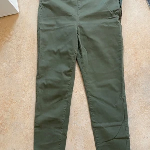 Olivgröna chinos från Lindex - Snygga olivgröna chinos från Lindex i storlek 44. Byxorna har klassisk passform med dragkedja och knapp framtill. Tillverkade i mjuk bomull som känns skön mot huden. Perfekta för en avslappnad och stilren look.