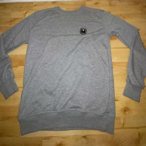 Grå sweatshirt med Palm Angels märke  - Grå sweatshirt från Tropical med svartvit palm-logo på bröstet. Klassisk rund halsringning och ribbade muddar vid ärmslut och nederkant. Tillverkad i mjuk bomullsmix som är skön att ha på sig. Perfekt för en chill och stilren look.