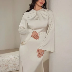 Lång ljus klänning med vida ärmar - Elegant långklänning från shein i ljus champagnefärg. Klänningen har vida långa ärmar, draperad detalj vid halsen och är tillverkad i ett glansigt satintyg. Perfekt för dig som vill sticka ut med en stilren och trendig look.