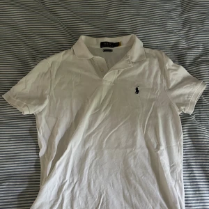 Vit pikétröja från Polo Ralph Lauren - Vit pikétröja från Polo Ralph Lauren i bomull med klassisk krage, korta ärmar och broderad logga på bröstet. Modellen är slim fit och har knappar vid halsen. Perfekt för en clean och stilren look. Storlek M fint skick. 