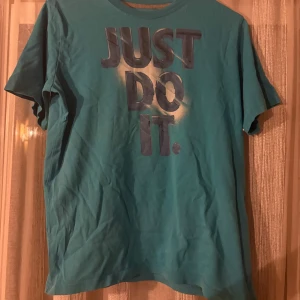 Turkos Nike t-shirt med tryck XL - Nike t-shirt i turkos med stort 'JUST DO IT.'-tryck på bröstet. Klassisk rund hals och korta ärmar. Skön passform och tillverkad i mjuk bomull, perfekt för en sportig och avslappnad stil.