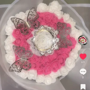 Silverfärgad ring med krona och fjärilar - Unik silverfärgad ring med kronformad detalj och gnistrande stenar, presenterad i en bukett av vita och rosa rosor med dekorativa silvriga fjärilar. Perfekt för dig som vill sticka ut med något riktigt speciellt.