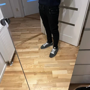 Svarta Nudie jeans - Svarta jeans från Nudie med klassisk femficksdesign och diskret broderad bakficka. Modellen är tilted Tor 31/32 och sitter snyggt längs benen. Jeansen är tillverkade i stretchig bomull för extra komfort och har svarta sömmar som smälter in i tyget.