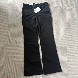 Kostymbyxor Bershka - Stilrena svarta kostymbyxor från Bershka med raka, vida ben och pressveck. Byxorna har hällor för bälte och klassisk stängning fram. Helt nya med prislapp. Storlek 34/XS