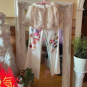 Pants No°1 - Unika shorts i ljusbeige med volangkant och knäppning i midjan. Materialet har en glansig sidenkänsla och shortsen har en flowy, omlottliknande form. Perfekta för dig som gillar en söt och lekfull stil med extra volym och rörelse.