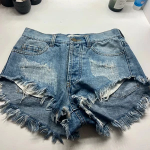 Blå slitna jeansshorts Rxxxx Studio - Säljer ett par blå jeansshorts från Rxxxx Studio i storlek S. De är högmidjade med fransig kant, slitna detaljer och knappar framtill. Klassisk femficksmodell i denim som ger en cool och avslappnad vibe.