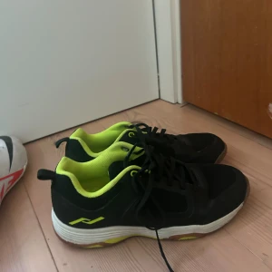 Svarta sneakers med neongul insida - Säljer ett par svarta sneakers från Rucanor med neongul insida och detaljer. Skorna har svart mesh och syntetmaterial på ovandelen, vita sulor med gula inslag och klassisk snörning. Perfekta för träning eller vardagsstil.