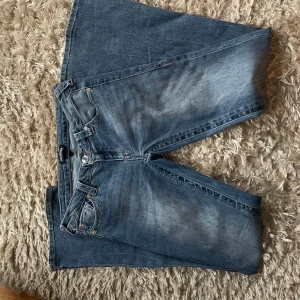 True Religion bootcut jeans blå, stl 28 - Säljer ett par klassiska blå jeans från True Religion i modellen bootcut. Jeansen har ikoniska bakfickor med broderad logga, snygga kontrastsömmar och silverfärgade nitar. Tillverkade i jeansmaterial med en skön passform och normal midja. As snygga rosa detaljer🩷pris kan diskuteras!