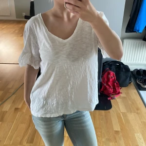 Vit blus med spetsärm från M&S - Säljer en luftig vit blus från M&S Collection med v-ringning och korta ärmar med broderad spetskant. Toppen är i mjuk bomull och har en avslappnad passform som känns chill och somrig.