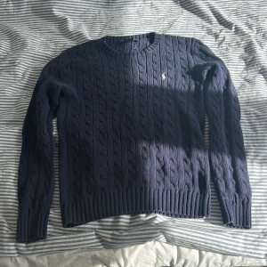 Mörkblå kabelstickad tröja Ralph Lauren - Kabelstickad mörkblå tröja från Ralph Lauren i 100% bomull. Väldigt bra skick ett litet hål bak vid nacken inget som syns 