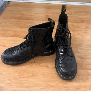 Dr. Martens 1460 Pascal svarta boots - Svarta Dr. Martens 1460 Pascal boots med unik vågig struktur på lädret, klassisk gul söm runt sulan och snörning framtill. Grov sula och rund tå ger en cool och robust look. Perfekta för dig som vill sticka ut med dina skor.