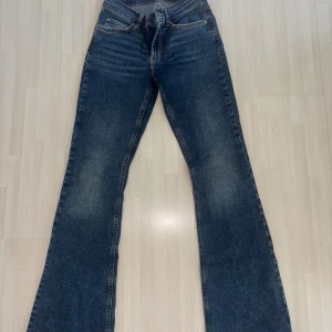 Blå bootcut jeans med utsvängda ben - Snygga blå jeans med bootcut-modell och klassisk femficksdesign. Jeansen har en mörk tvätt med lätt slitning framtill och är tillverkade i ett robust denimtyg. Perfekta för dig som gillar en retroinspirerad look med utsvängda ben.