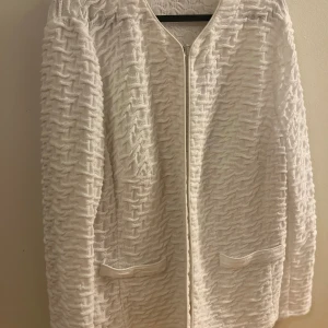 Vit stickad cardigan jacka/kofta Frank Walder - Vit cardigan jacka/kofta från Frank Walder med snyggt stickat strukturmönster och två fickor framtill. Jackan har lång ärm och stängs med en diskret hake. Perfekt för dig som gillar en stilren och fräsch look.
