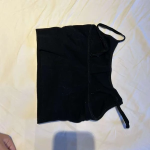 Svart croppad linnetopp vet inte vart ifrån  - En svart croppad linnetopp med smala axelband och enkel design. Toppen har en tight passform och är perfekt att styla med jeans eller kjol. Materialet känns mjukt och stretchigt, vilket gör den bekväm att bära hela dagen.