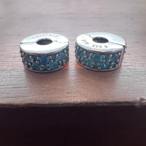 Två klämstopp till Pandora armband - Två stycken turkosa klämstopp i silver till Pandora armband. Så gott som nytt. Använt färre än 10 gånger. (Armband ingår ej i priset)