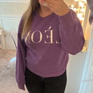 Lila sweatshirt LÈON från Gina Tricot - Lila sweatshirt från Gina Tricot med trycket 'LÈON' i vitt framtill. Tröjan har rund hals, ribbade muddar och en relaxed passform. Perfekt för dig som gillar en enkel men snygg look. Materialet är mjuk bomullsmix.