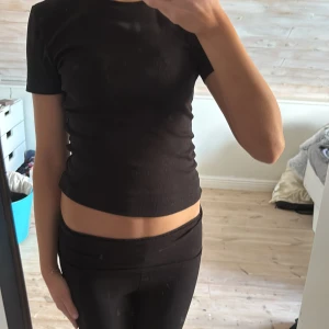Svart croppad t-shirt - En enkel svart croppad t-shirt med rund hals och korta ärmar. Toppen har en tight passform och är perfekt att matcha med jeans eller kjol. Materialet känns mjukt och stretchigt, vilket gör den bekväm att bära hela dagen.