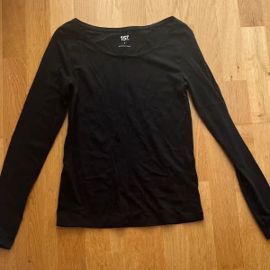 Svart långärmad topp från 157 - En svart långärmad topp från 157. Modellen har rund halsringning och en slim passform som sitter snyggt på kroppen. Perfekt att styla med jeans eller kjol för en clean look.