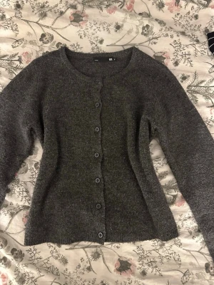 Mörkgrå kofta med knappar - Mysig mörkgrå kofta från H&M med rund hals och knäppning framtill. Koftan är stickad och har långa ärmar, perfekt för kyliga dagar. Enkel och stilren design som passar till många olika outfits.