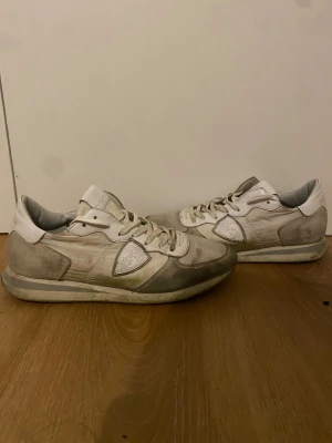 Philippe Model vita sneakers  - Säljer ett par vita Philippe Model sneakers med grå paneler och logotyp på sidan. Skorna har snörning, rund tå och platt sula. Materialmix av skinn och syntet, med mesh på ovansidan. Perfekt för dig som gillar stilrena och klassiska sneakers.