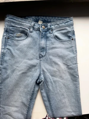 Ljusblå high waist jeans från Recap - Säljer ett par ljusblå jeans från Recap med hög midja och klassisk femficksdesign. Jeansen har vida ben (Bootcut) och en snygg vintage-wash. Märkesdetaljer finns både fram och bak, och materialet är mjukt denim i bomull. Perfekta till sneakers eller boots.