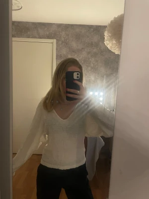 Vit långärmad blus med v-ringning - Säljer en vit blus från Lindex med v-ringad hals och långärmade, lätt puffiga ärmar. Materialet är krinklat och ger en cool textur. Passformen är normal och toppen är enkel att matcha med både jeans och kjol.