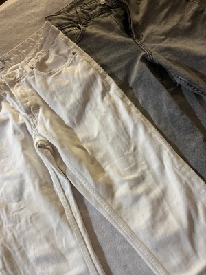 Vita och grå jeansbyxor - Två par jeansbyxor, ett par i vit och ett par i grå tvätt. Båda har klassisk femficksdesign och raka ben. Vita byxan har elastisk midja medan den grå har traditionell knapp och dragkedja. Perfekt för dig som gillar enkel och clean stil.  BÅDA FÖR 150 kr eller 1 för 75!🩶🤍
