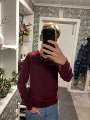 Vinröd bomullströja med v-ringning - Säljer en vinröd tröja i storlek S med v-ringad hals och långa ärmar. Tröjan är tillverkad i 100% bomull och har ribbade muddar vid ärmslut och nederkant. Enkel och stilren design som funkar till jeans eller andra favoritplagg.