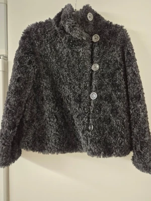 Teddyjacka - Mjuk och fluffig svart teddyjacka från Lindex med hög krage och stora knappar framtill. Jackan har långärmade ärmar och är perfekt för dig som gillar en chill och cozy stil. Materialet är syntet och ger en riktigt skön känsla.